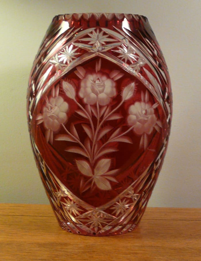 The flower motif is etched into the red stain, while the bordering pattern is pressed into the glass. The vase is about 12" tall.