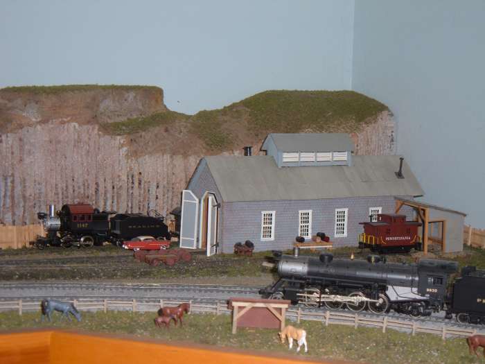 A 2-8-2 steamer rounds the bend on the dual track mainline. The engine house is off one of the branch lines.