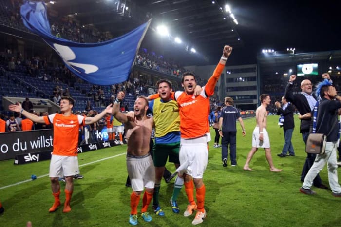 Marco Sailer (waving flag), David Salfeld and Dominik Stroh-Engel (left arm extended) celebrate with fans inside Bielefelder Alm on May 19, 2014. SV Darmstadt 98 knocked out DSC Arminia Bielefeld on away goals to return to the 2. Bundesliga.