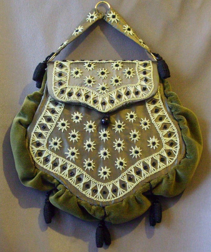 This bag consists of a buckram frame, covered in embroidered silk taffeta. Tiny black glass pearls from a late Victorian mourning dress highlight the design. The outside is covered in velvet. A bag such as this would have been "hooked" into the waist