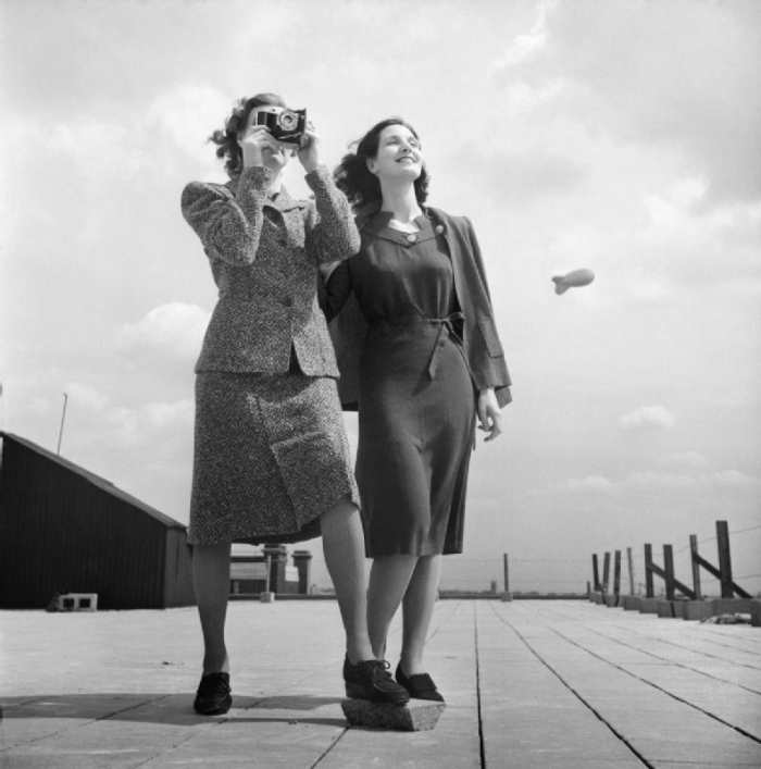 1943: The simple dresses of wartime featured short hemlines. There is a barrage balloon in the background.