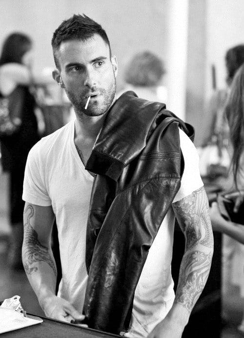 hier combineert Maroon 5 ' s Adam Levine een effen wit T-shirt met een donker leren jack. In dit geval helpt zijn stoppels echt de look te voltooien. 