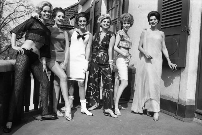 A wide variety of mid 60s styles including bouffant hair, short skirts, go-go boots, middriff top, and Bermuda shorts.