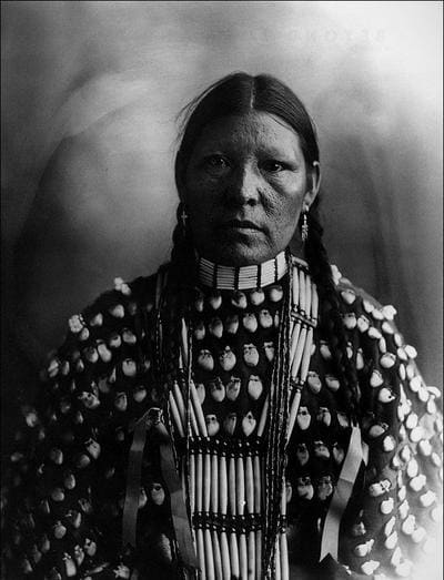 Freckle Face, an Arapaho woman in a shirt decorated with elk teeth, wearing hairpipe jewelry.