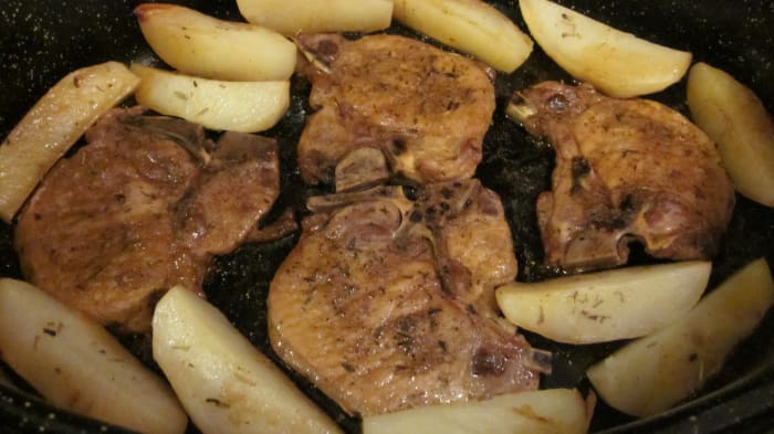 Pork chops are hot, tender and ready to serve with potatoes sprinkled with rosemary leaves.