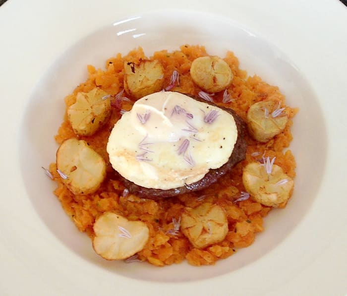 Buffalo and beef burger on carrot mash with deep-fried potato crowns, poached egg and chive flowers.