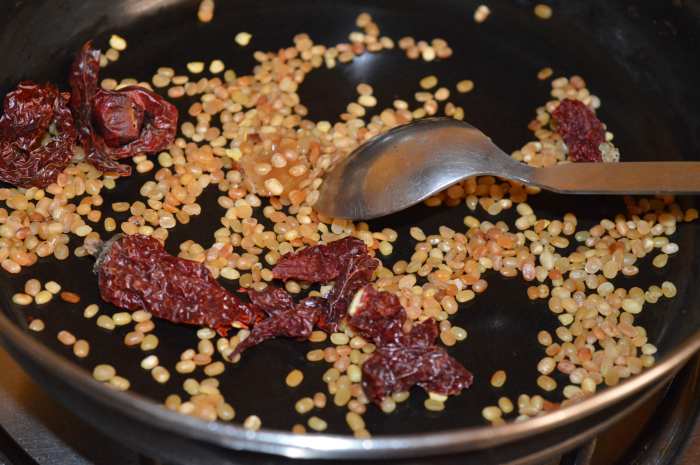 Step two: Add broken dry red chilies and hing to the pan. Let them get crispy from the residual heat. Also, add tamarind if you are not soaking it in water. Set the pan aside to cool.