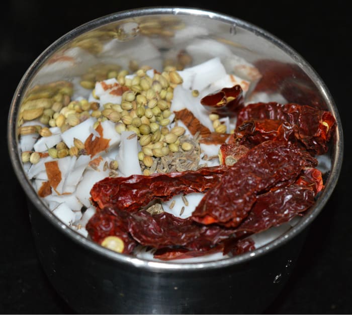 Step three: In the meanwhile, make masala paste for the gravy. Take grated coconut, cumin seeds, coriander seeds, dry red chilies, hing powder, and raw rice in a mixer jar. Grind, adding water to get a near-smooth paste.