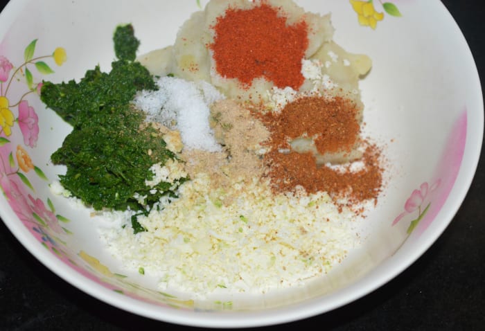 Step four: Add the leafy greens paste, grated paneer, mashed potatoes, red chili powder, spice powder or garam masala powder, raw mango powder, and salt. Mix well to prepare a firm dough.