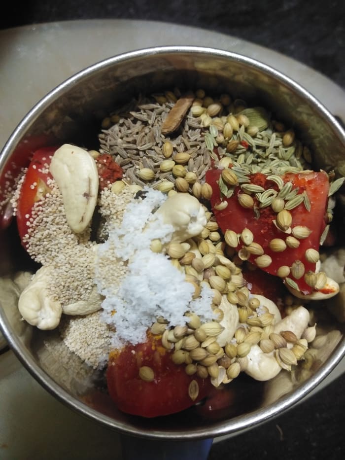 In a blender, add cumin seeds, fennel seeds, coriander seeds, cinnamon, cardamom, clove, cashew nuts, tomatoes, green chili, ginger, poppy seeds, turmeric powder, red chili powder, and salt.
