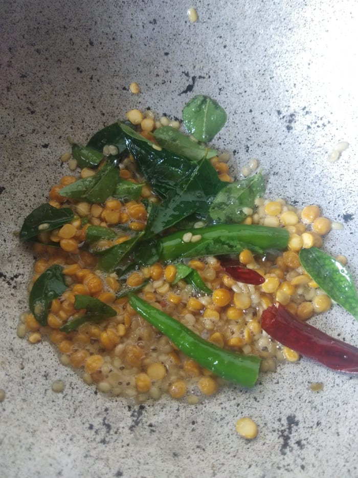 Add broken red chilies, green chili, curry leaves, and hing. Fry over low flame till dal turns golden brown and curry leaves become crispy. Do not burn. Set aside to cool.