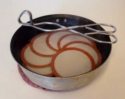 Gently simmer the lids (don't boil!), or set them in a small pan and pour on boiling water to cover, in order to scald them.