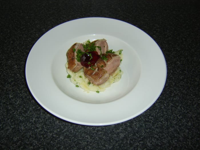 The pan-fried duck breast is rested before being sliced and served on the bed of mash, garnished with parsley and red currant jelly.