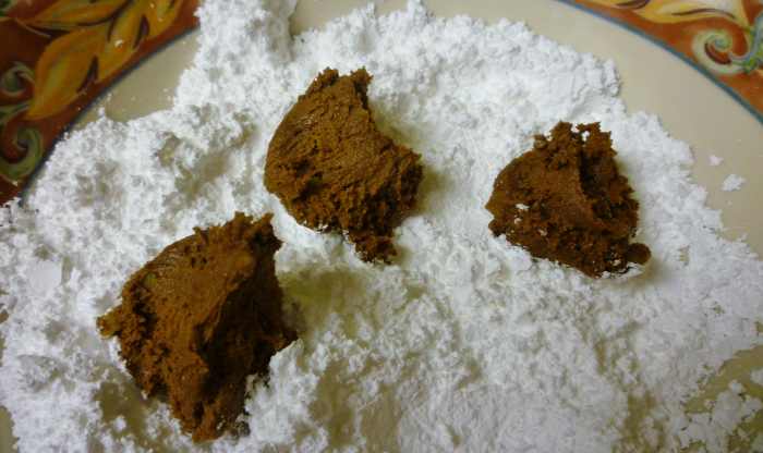 Dropping bits of the cookie batter into powdered sugar and then rolling into a ball shape.