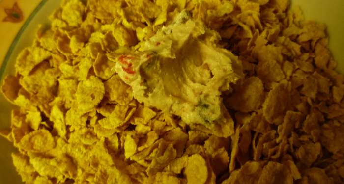 Dropped teaspoonful of cookie dough into cornflakes where they will be rolled into a ball shape.