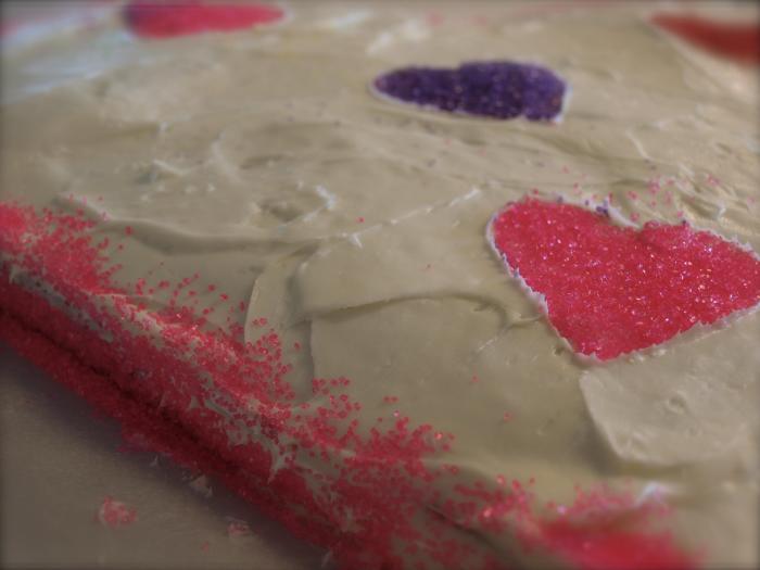 Using decorations of your choice, decorate the cake. To get the glitter hearts, I used a heart-shaped cookie cutter and gently laid it on the cake surface. Then I added glitter to the center of the cutter.
