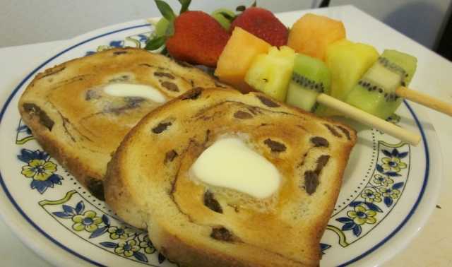 This serving suggestion for a light breakfast includes two fruit kabobs served with toasted, buttered raisin bread.