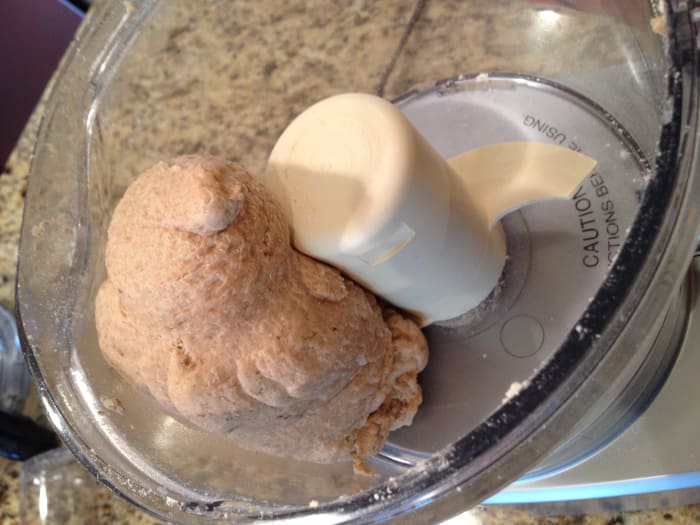 Combine hot water with olive oil in a measuring cup. Turn the food processor on and gradually pour in the liquid until the mixture forms a sticky ball. Add additional water or flour if needed.