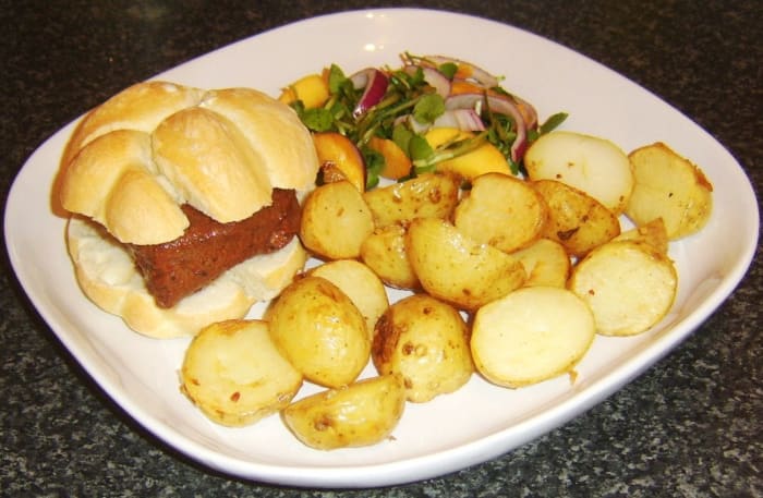 Ostrich steak in marrakesh sauce is served on a bread roll with deep fried potato halves and a peach and watercress salad