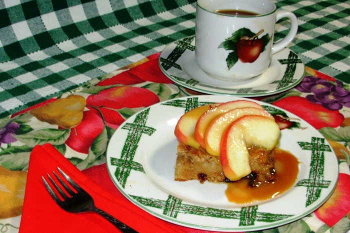 A slab of bread pudding topped with sauted apple slices and drizzled with caramel sauce.