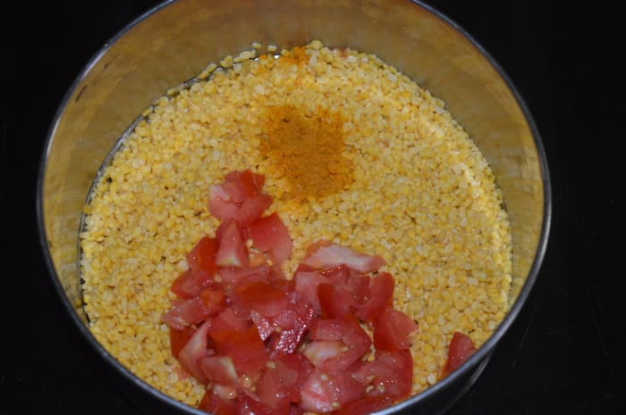 Step five: Wash de husked split mung beans in water. Add fresh water, chopped tomato, some salt, and turmeric powder. Cook them in a pressure cooker. This is for making the soup.