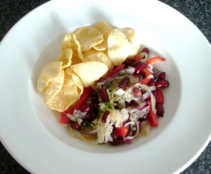 Kwalstsalade met uien, chilipepers en bonen geserveerd met limoen en koriander poppadoms