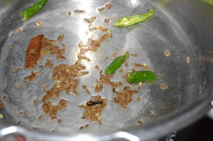 Step two: Heat oil in a cooker base or a deep-bottomed pot. Throw in cumin seeds, slit green chilies, cloves, and cinnamon stick. Saute until cumin sizzles.