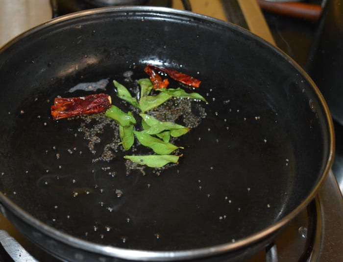 Step two: Heat oil in a deep-bottomed pan. Add mustard seeds. Let them crackle. Throw in broken red chilies and green chilies(optional). Also add curry leaves. Saute for 10 seconds on low heat.