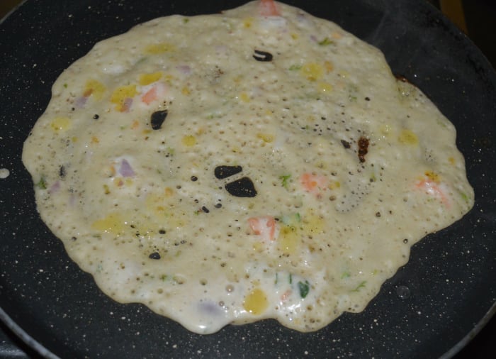 Step five: Heat a pan, preferably a non-stick pan. Grease it with ghee or oil. Pour 1 1/2 ladles of batter in the center. Spread it to make a pancake. Add a few drops of ghee or oil on the top.