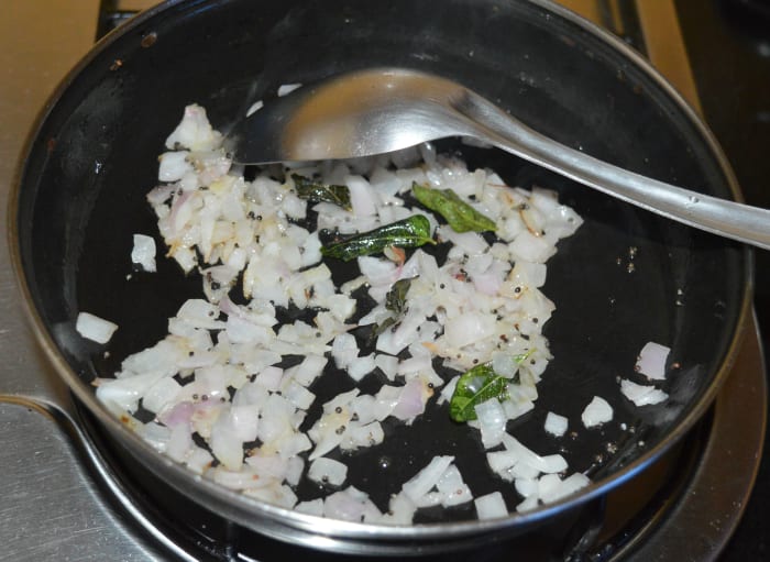 Step three: Heat oil in a deep-bottomed pan. Throw in mustard seeds. Let them crackle. Add chopped onions. Saute until onions are transparent. Add curry leaves and hing powder.