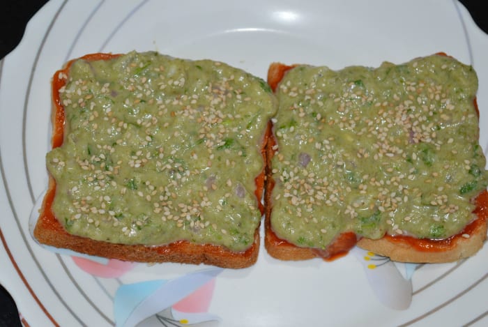 Step four: Generously spread the cheese-moong dal mixture on them. Also, add some white sesame seeds on the top. This will give crunchiness to the toast.