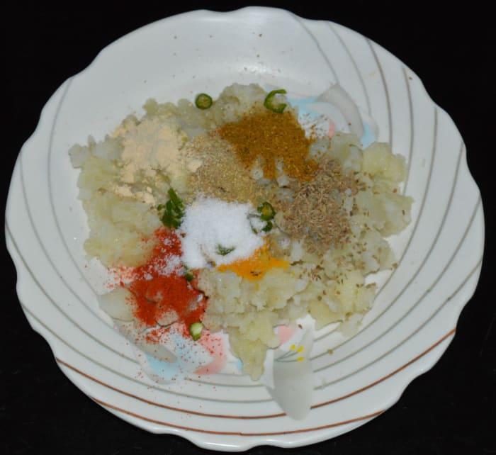 Step two: Place mashed potato, red chili powder, chopped green chilies, turmeric powder, carom seeds, garam masala powder, sugar, coriander powder, and salt in another bowl. Mix them thoroughly, so that there are no lumps. This is the stuffing.