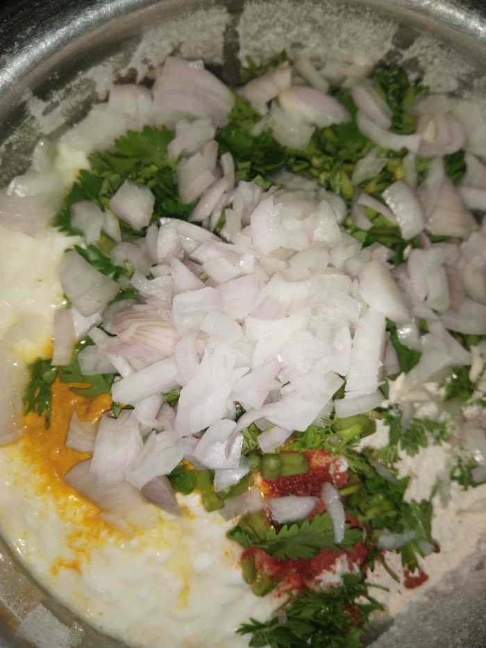 Add wheat flour, yogurt, turmeric powder, red chili powder, finely chopped green chili, coriander leaves, sugar, and salt.