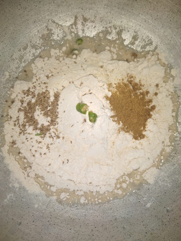 In a bowl, add wheat flour, salt, carom seeds, green chilies (optional), asafoetida (hing) and cumin powder.
