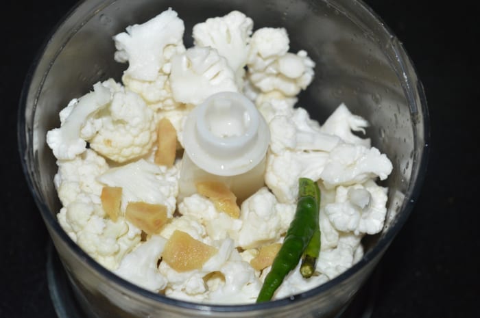 Step two: Wash cauliflower florets. Put them into a food processor along with ginger and green chilies. Finely chop them.