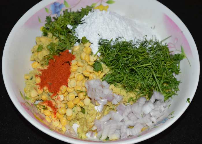Step two: Add chopped coriander leaves, dill leaves, onions, rice flour, red chili powder, soaked chickpeas, and salt. Mix well. If you feel the dough is not dry, add some more rice flour. Mix once again.