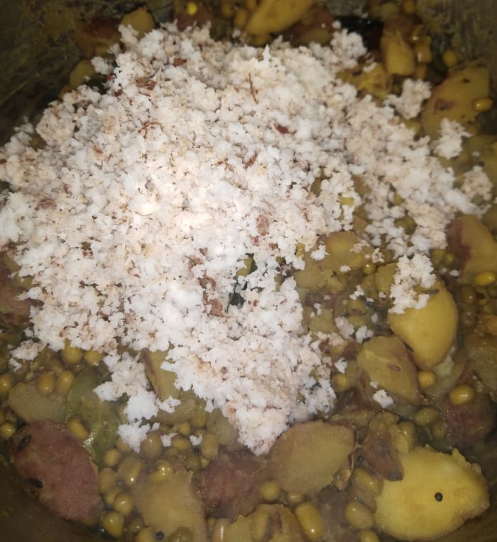 Once everything is cooked and tender and the water dries up completely, lower the flame and add fresh grated coconut.