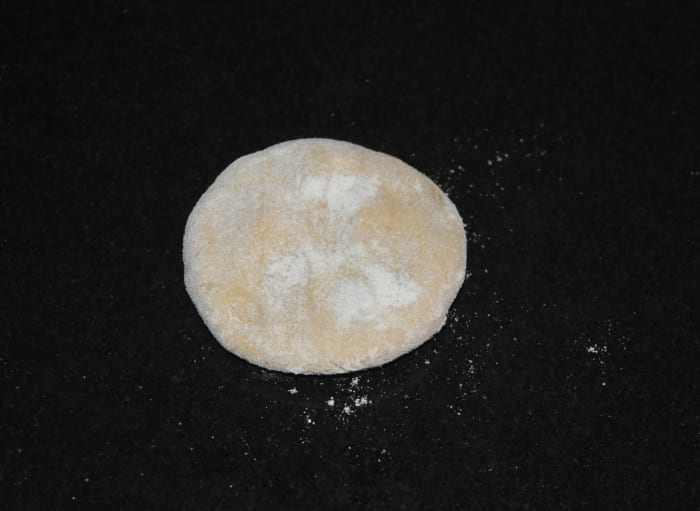 Step four: Gently knead the dough once again. Take a lemon-sized dough portion and shape it like a patty. Make a small disc out of it. Use wheat flour for dusting while rolling.