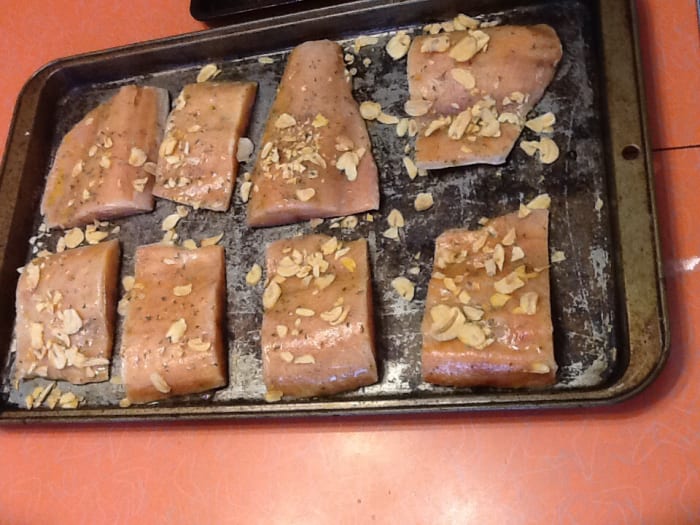 Take a pastry brush and brush the salmon fillets all over with the seasoning. Sprinkle the garlic flakes and parsley on top.