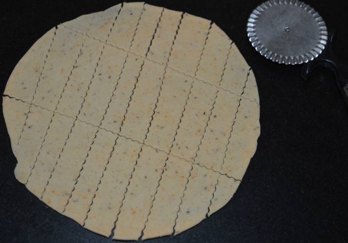 Step two: Take the first dough portion. Make a patty out of it. Roll it out to make a thin disc. With a knife, cut rectangular strips.
