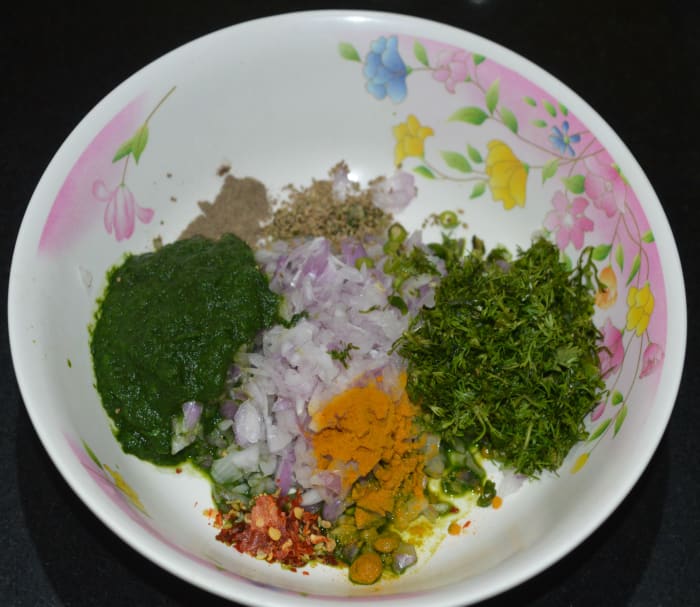 Step two: Add the green paste to a large mixing bowl. Add chopped onions, grated ginger, chopped coriander leaves, green chilies, chili flakes, carom seeds, pepper powder, turmeric powder, jowar flour, and salt.
