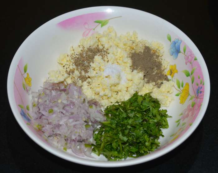 Step two: In a mixing bowl, add crumbled paneer, chopped onions, coriander leaves, carom seeds, pepper powder, and salt. Mix well. This is the stuffing for the parathas.