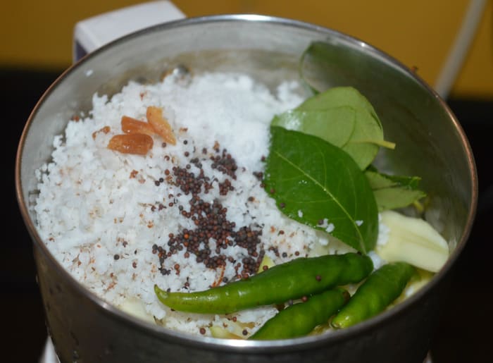 To a mixer jar, add mango, grated coconut, green chilies, mustard seeds, hing powder, curry leaves, and salt. Grind, adding some water, to get a near-smooth paste. Transfer it to a bowl.