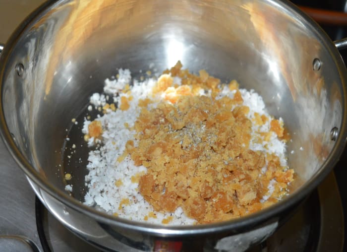 Step two: Heat a deep-bottomed pan containing jaggery powder, cardamom powder, and grated coconut. Add a few drops of water to loosen the mixture.