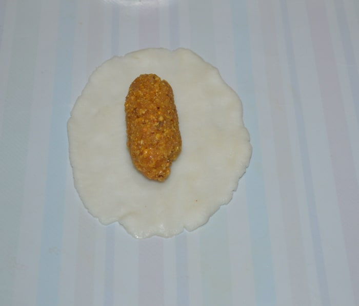 Take one of the dough portion and place on the greased plastic sheet or board. Gently pat it with greased fingers to extend it on all sides, as shown in the image. Don't make it too thin. Place a stuffing portion in the center.
