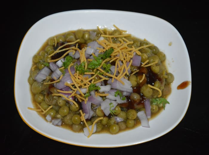 Pour 2-3 ladles of piping hot ragda on the patties. On that, add sweet and sour chutney and green chutney. Garnish with fine sev, chopped onions, and chopped coriander leaves. Place a spoon for eating.