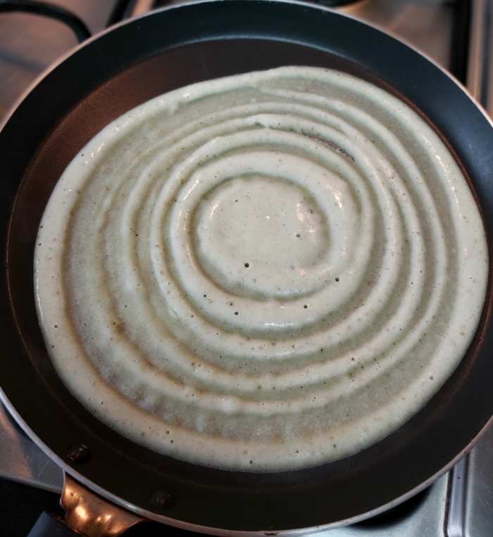 Pour a ladleful of batter in the center of the pan. Gently spread the batter in a circular motion, forming a thin dosa.