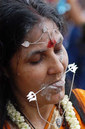 A women devotee who has opted to have her penance done by having a metal skewer pierce through her mouth and part of forehead during Thaipusam celebration