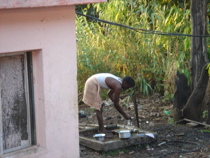 This man is standing and leaning over a spigot to wash dishes in India.