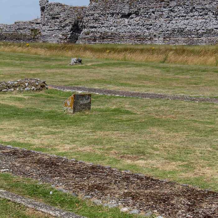 All that remains of the 12th century chapel at Richborough are these foundations and some concrete markers in the foreground. The north wall of the Roman fort stands in the background beyond a trench